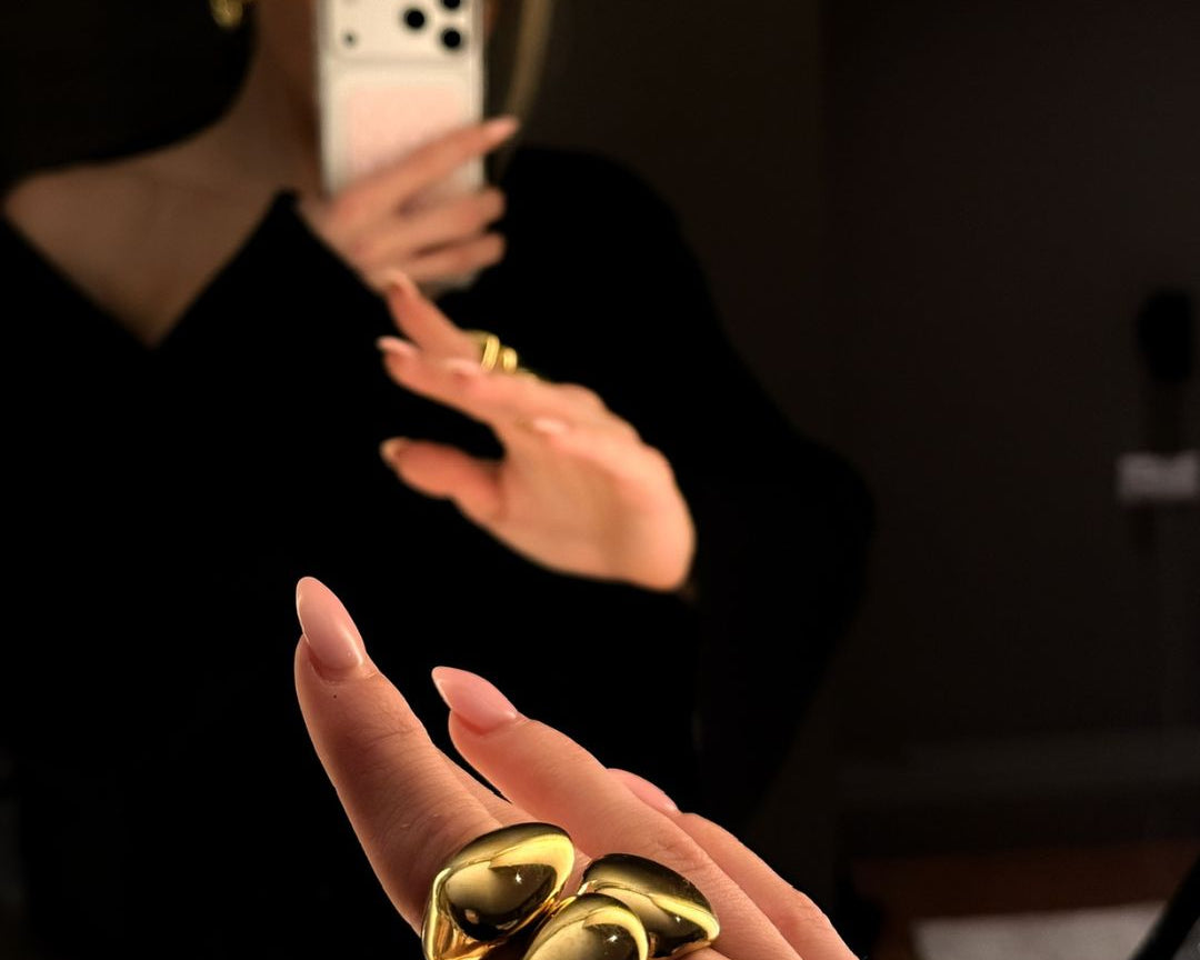 A blonde women making a picture in the mirror of her hand with the three golden rings stacked. 