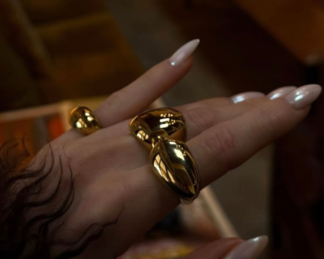 A photo of a hand with pearl nails wearing three golden rings.