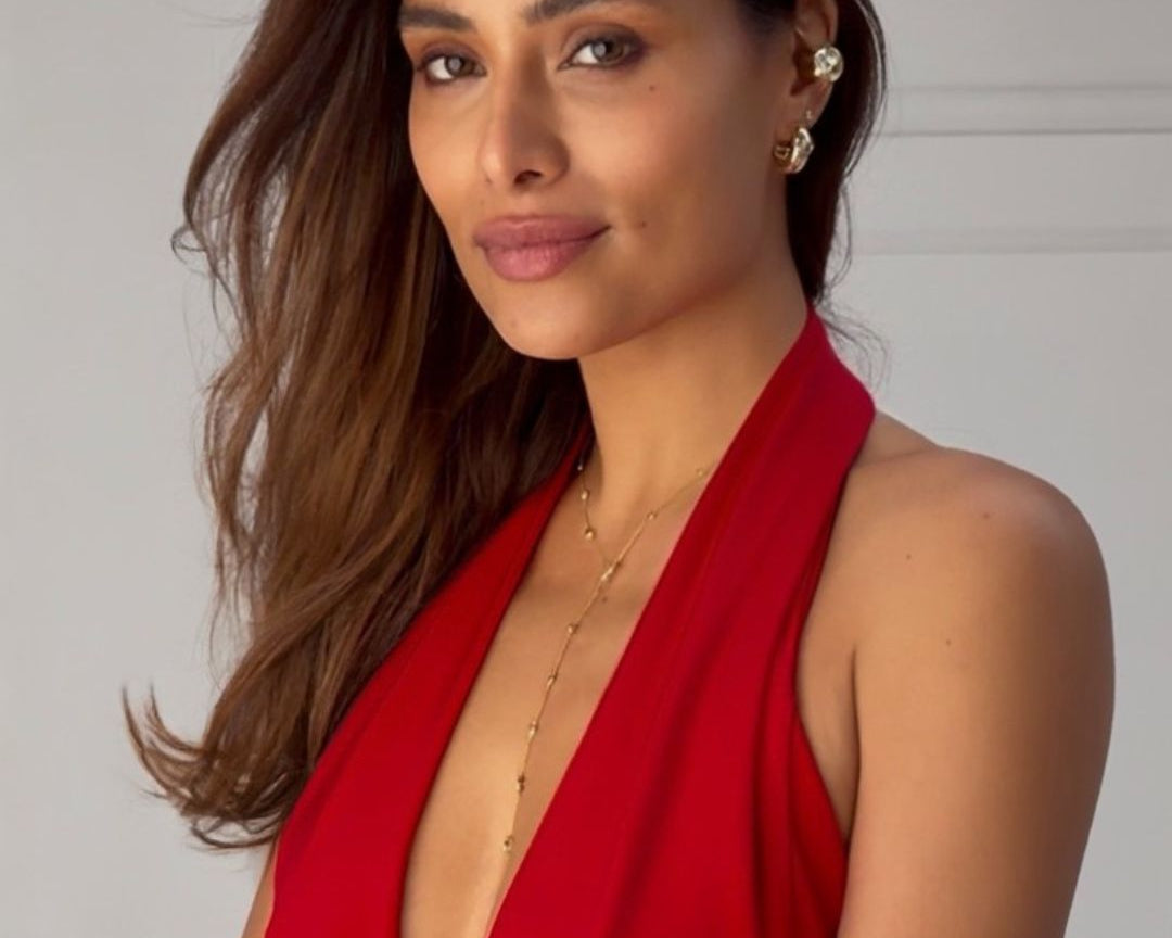 A brunette women in a red dress. She is wearing the gold ear cuff, earrings and necklace with heart. 