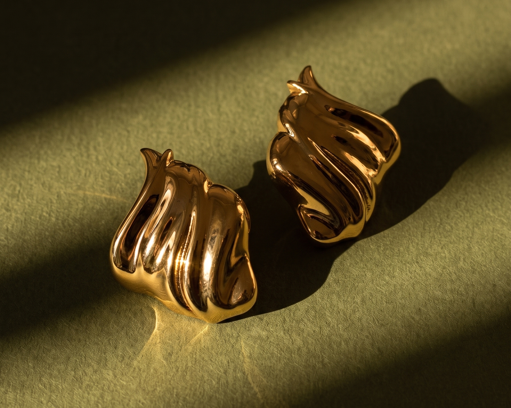 Gold plated sculptural earrings on green fabric