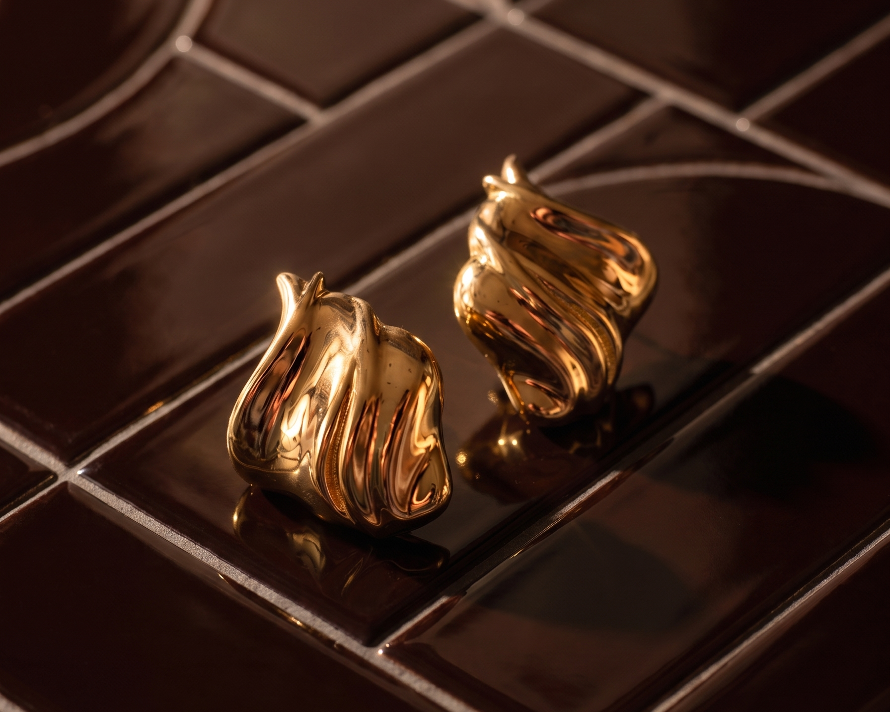 Gold plated sculptural earrings on a metal surface